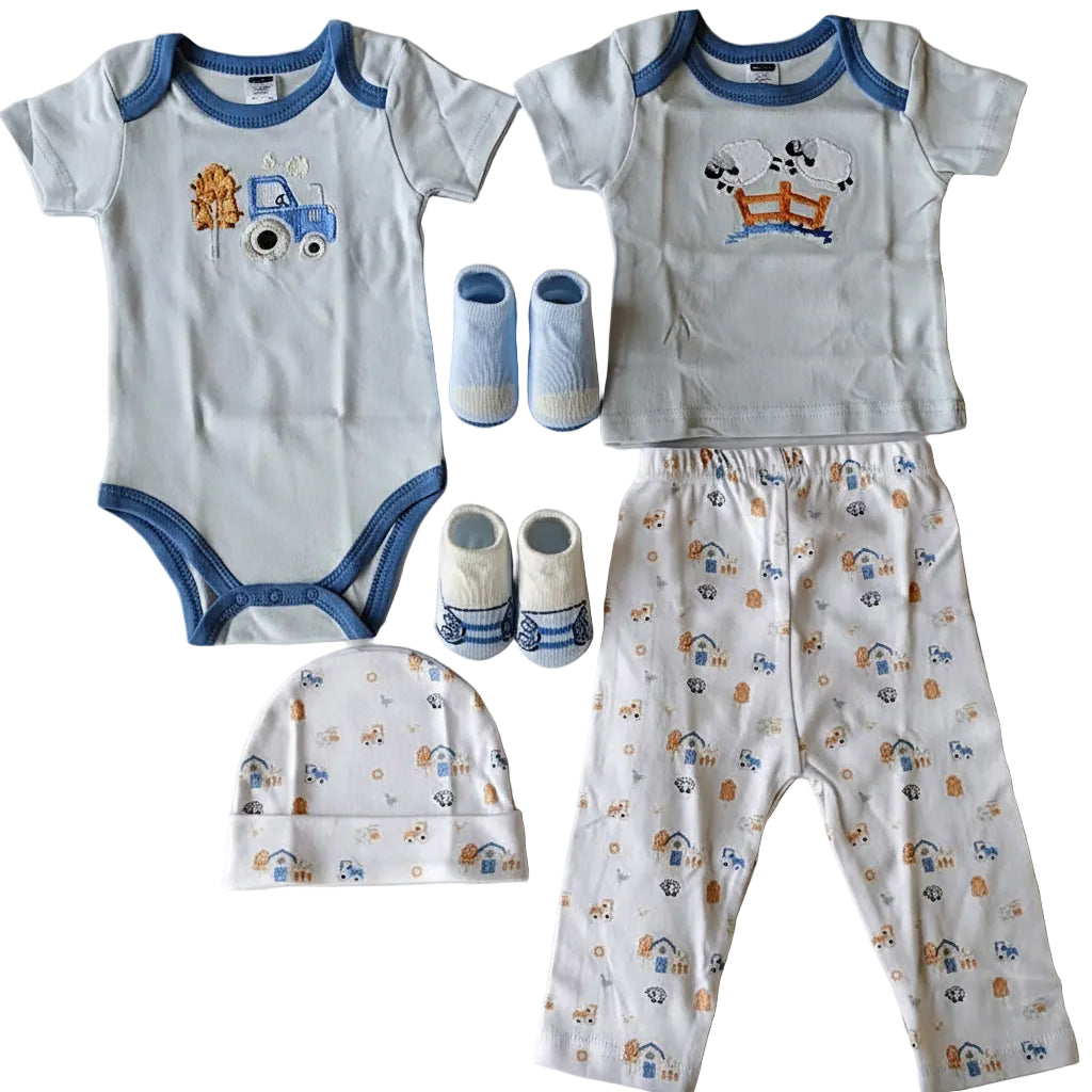 A baby clothing set laid flat on a light background, including a white short-sleeve bodysuit with blue trim and a cartoon truck graphic, a matching white short-sleeve top with blue trim and a cow graphic, white patterned pants, a white beanie with blue and orange print, and a pair of blue-and-white booties.