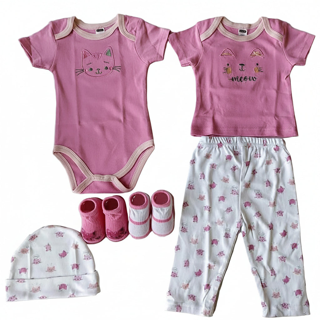 A baby clothing set laid out on a light background, including a pink short-sleeve bodysuit with a cat face graphic, a pink short-sleeve top with a small multicolor moon graphic, white leggings with pink bunny prints, pink booties, and a white beanie with a pink bunny pattern.