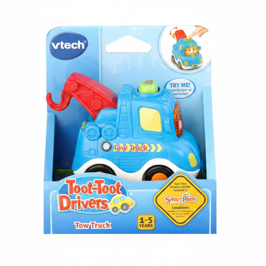 VTech Toot-Toot Drivers Tow Truck toy in its original retail packaging, featuring a blue toy truck with a red crane, yellow accents, and a light-up feature shown on the packaging insert.