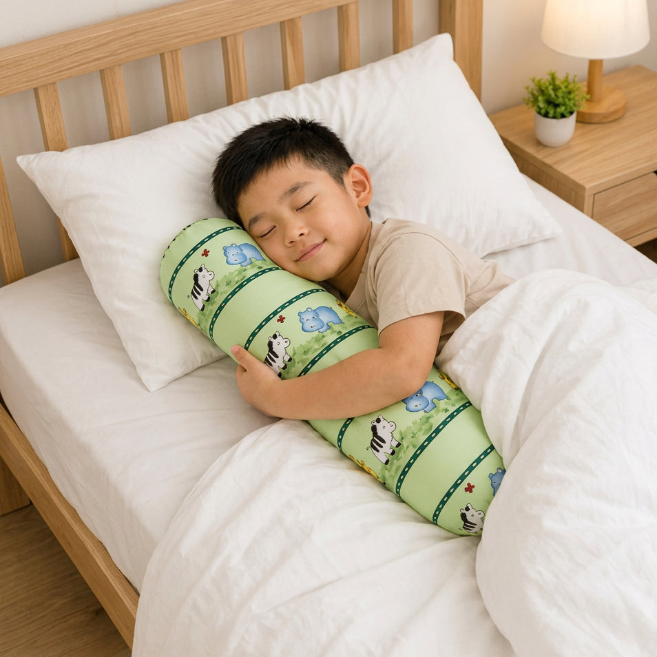 A young boy sleeping soundly on a wooden bed, hugging a long cylindrical bolster pillow. The pillow has a pale yellow background decorated with cartoon animal illustrations, including a zebra and a giraffe, separated by dark green stripes.