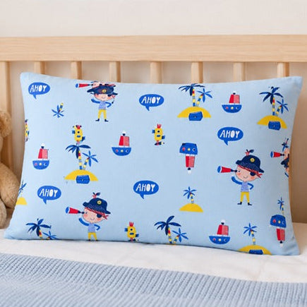 A rectangular baby pillow with a light blue background and a colorful pirate-themed print, displayed on a wooden bed next to a teddy bear.