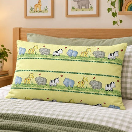 A rectangular decorative pillow with a yellow background and an animal print pattern of giraffes, zebras, hippos, elephants, and a crocodile, styled on a bed in a child's bedroom.